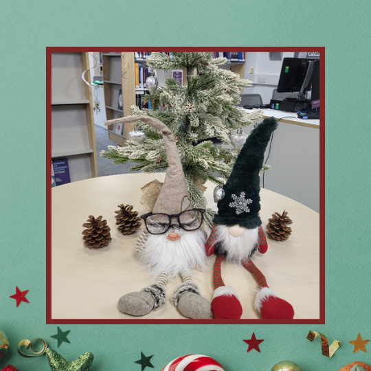 The background is green, the bottom of the image shows scattered Christmas decorations. In the middle, over the top, is a photo of MWL Libraries Christmas Gonks Magnus and Snorri.